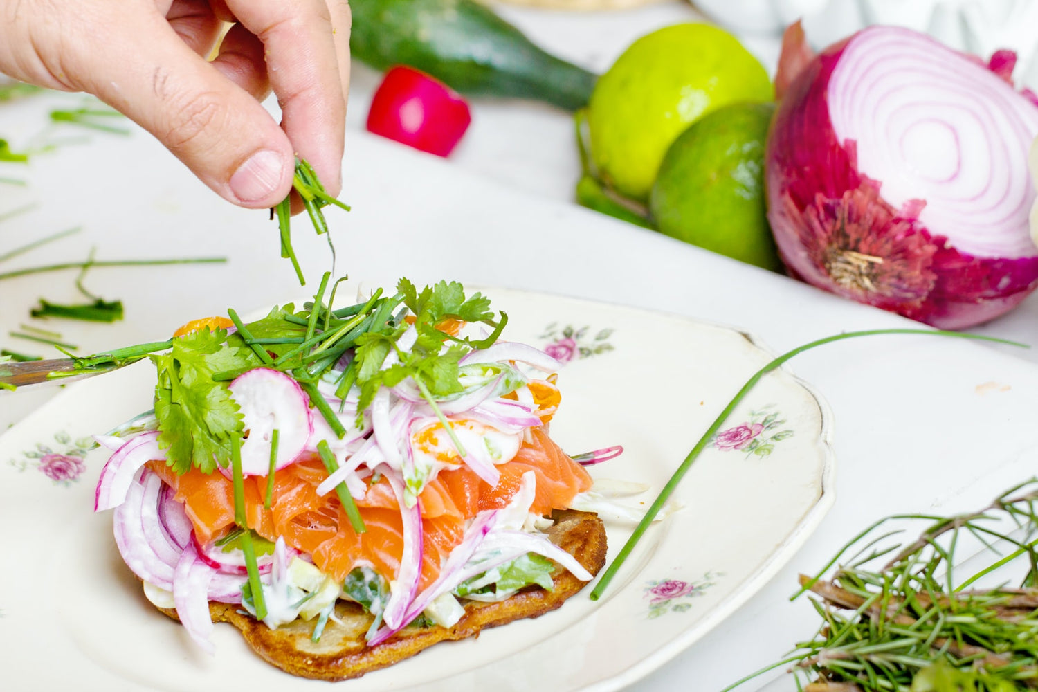 Teller mit Lachs, Zwiebeln und Kräutern, eine Hand streut Kräuter darüber