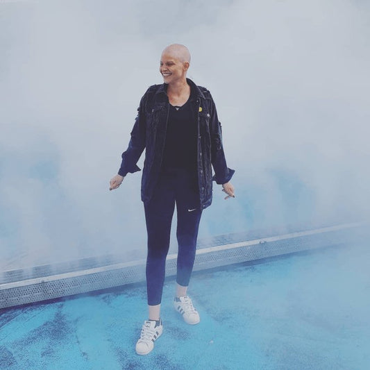 Brustkrebspatientin Carina mit ausgefallenem Haar vor Nebelwand, lachend